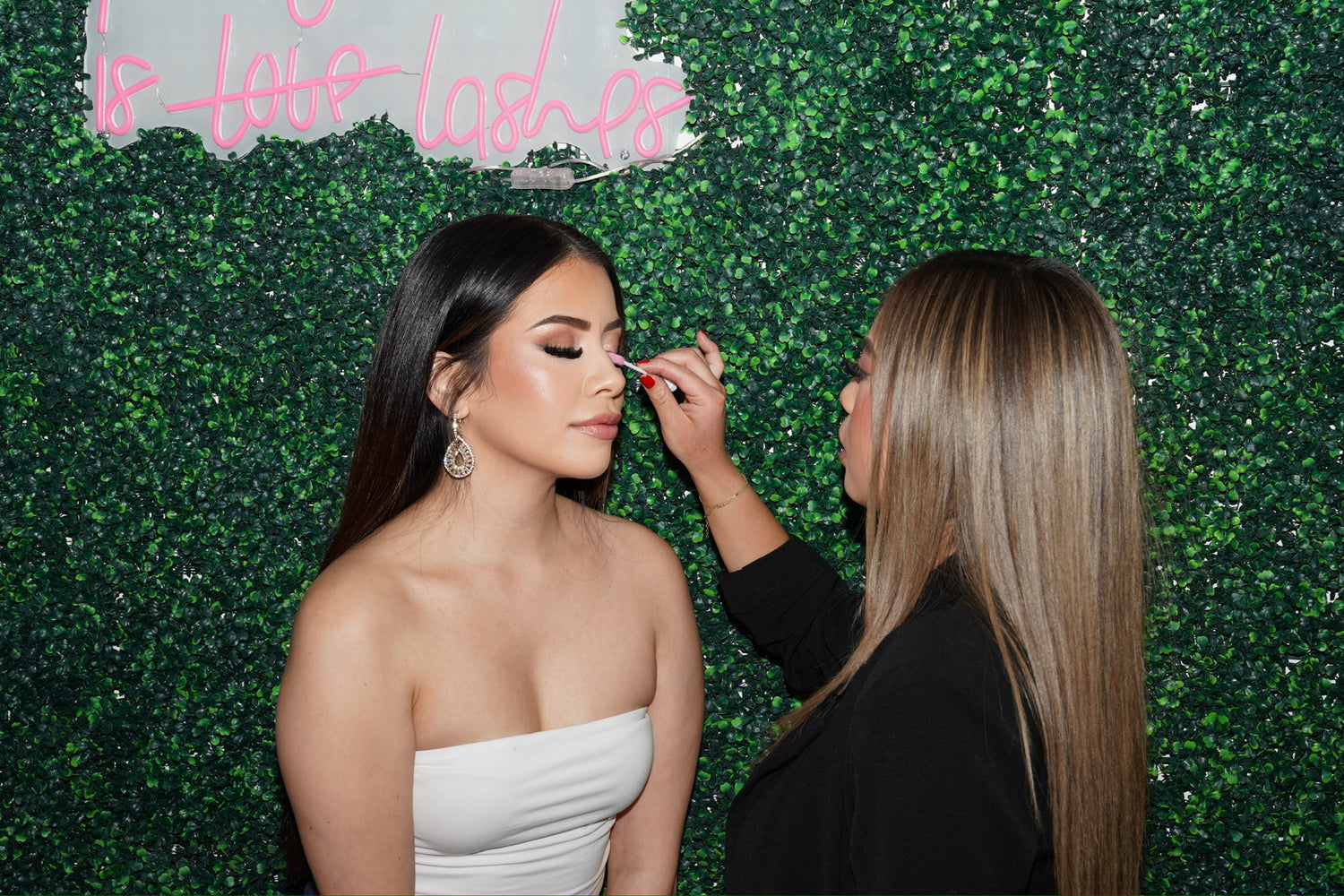 Makeup artist applying eyelashes to a model against a green leafy background